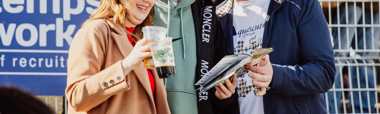 A small group of racegoers at Chepstow are stood huddled around a horse race card