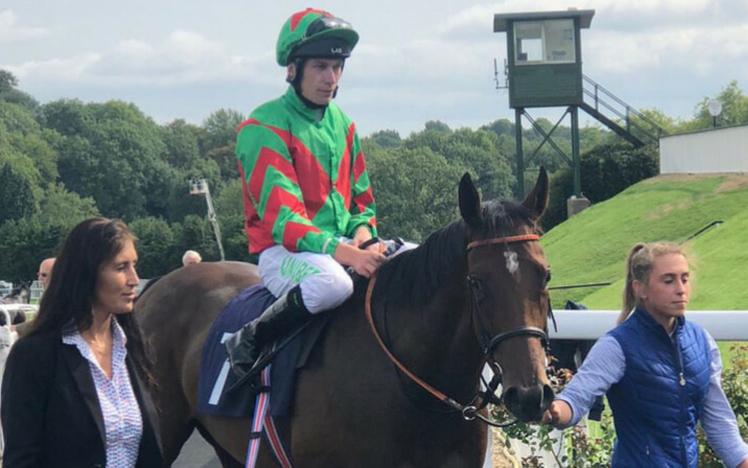 A Jockey on horseback is led around the parade ring by a handler.