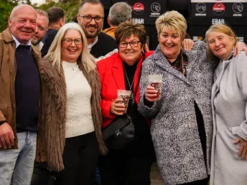Group of smiling racegoers enjoying drinks and posing together at Chepstow Racecourse on a lively raceday.