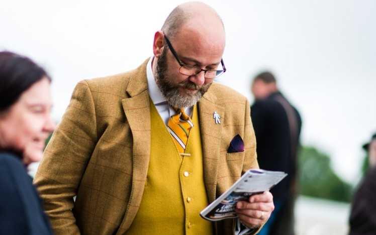 A well-dressed man checks his racecard and the runners and riders.