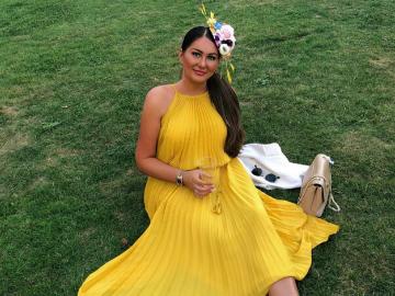 A beautiful woman in a yellow dress sits on the green grass at Chepstow Racecourse