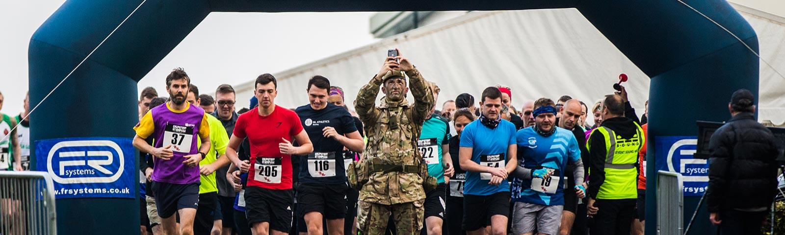 A soldier in camouflage takes a selfie as the stamped gets underway with lots of other competitors in standard running attire