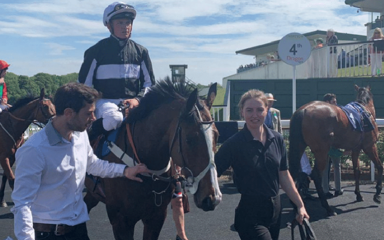 A Jockey on a horse is led from the racecourse by handler and trainer