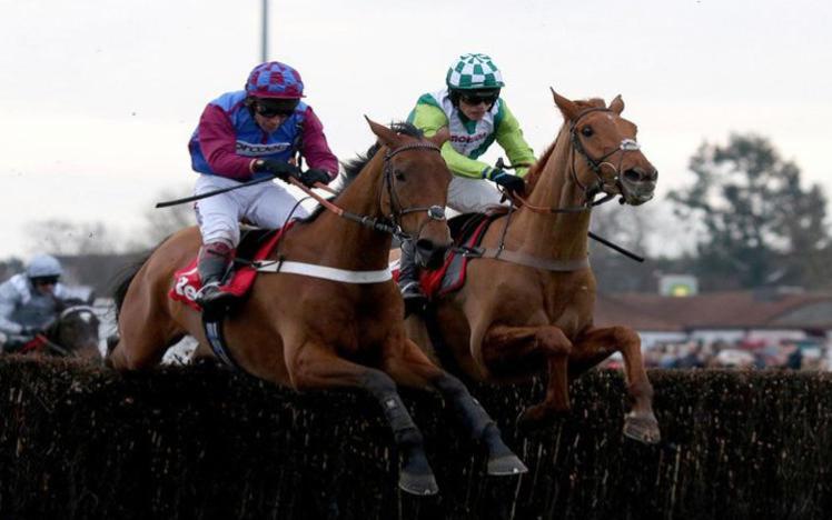 Two horses jumping a fence at Chepstow Racecourse.