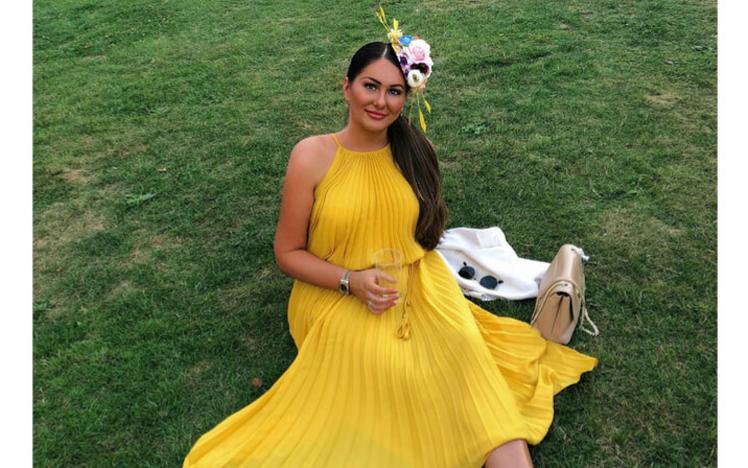 A beautiful woman in a yellow dress sitting on the green grass at Chepstow Racecourse
